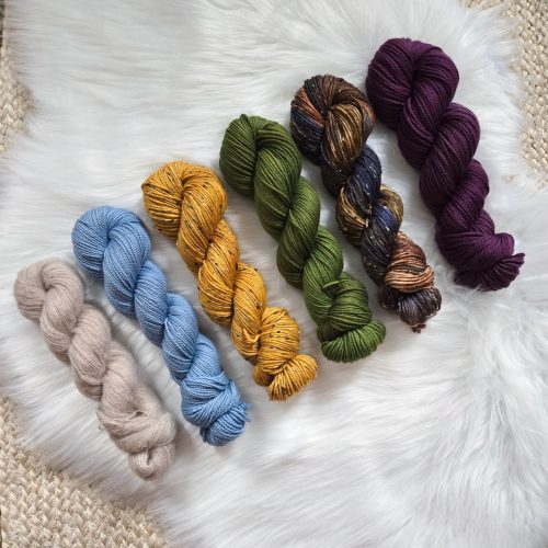 Skeins of beige, light blue, yellow, green, brown, and purple yarn.