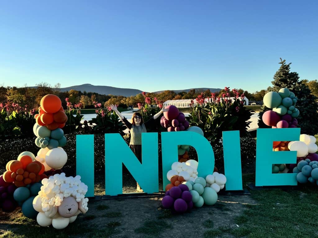 A woman standing behind big blue letters spelling the word INDIE.