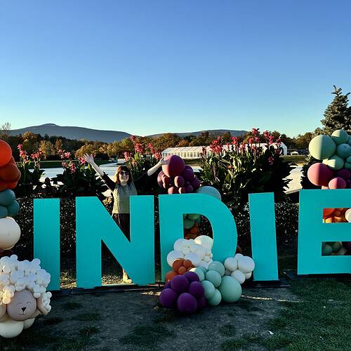A woman standing behind big blue letters spelling the word INDIE.