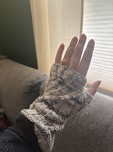 Light skinned woman wearing knitted fingerless gloves in different shades of grey