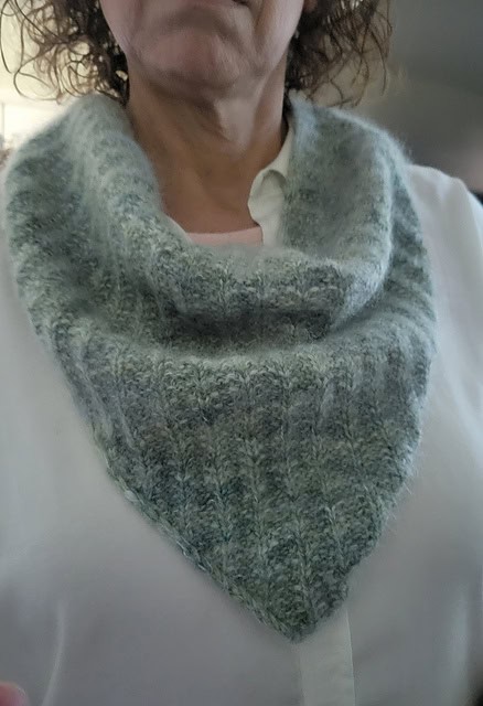Light skinned woman wearing a soft, ribbed knit bandana cowl in light green tones over a white shirt