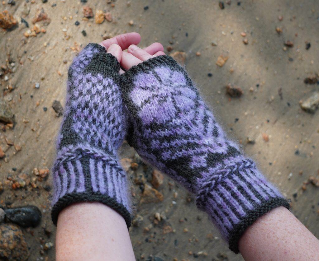 Light skinned woman wearing knitted fingerless mittens in the color purple