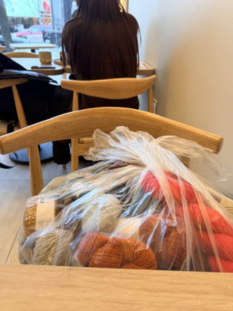 Skiens of yarn in a clear bag sitting on a chair in a coffee shop. 