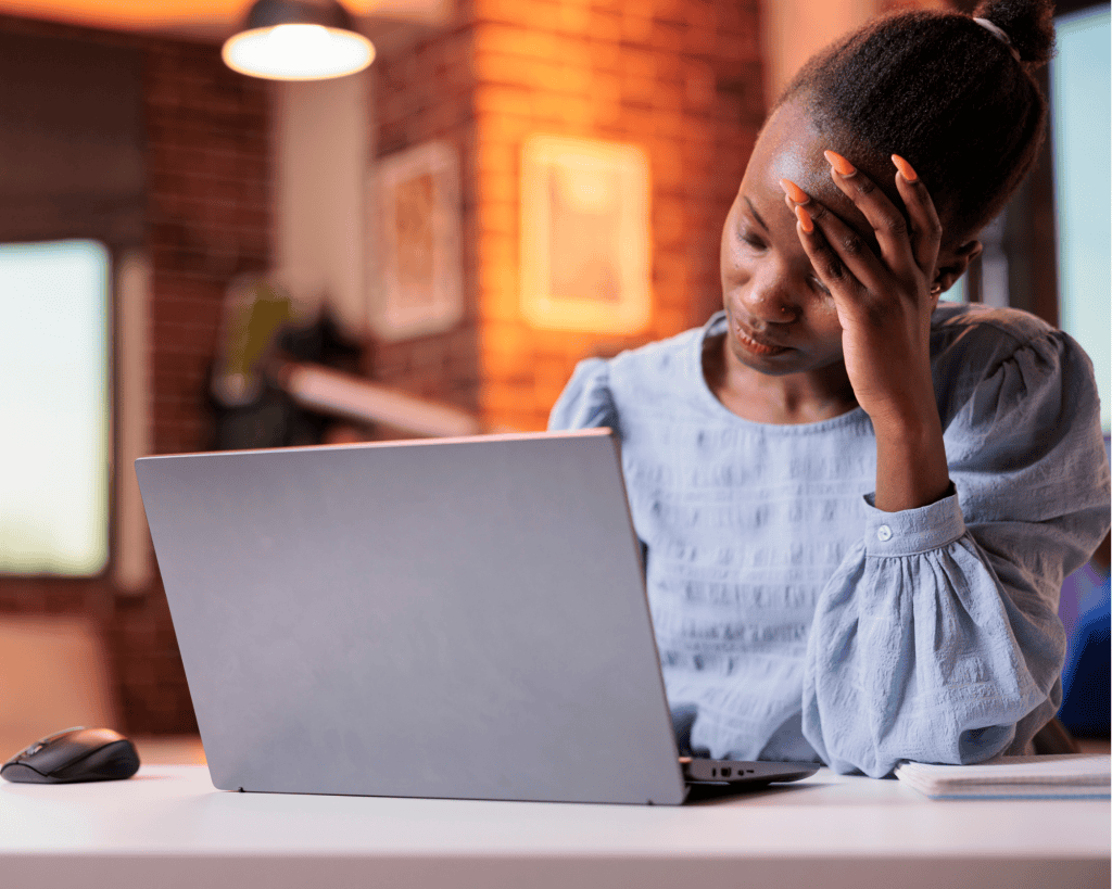 young dark skinned woman with blue blouse sitting in front of computer looking stressed