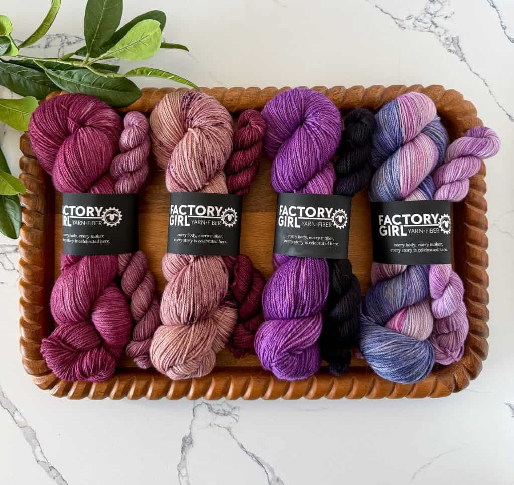 Purple, pink and jewel toned yarn on wood tray.