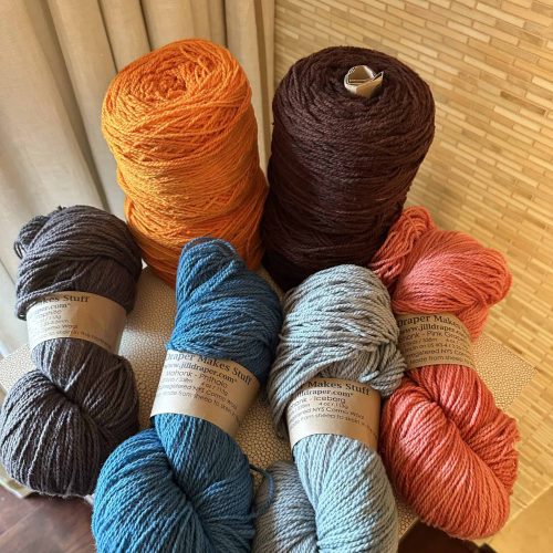 Eight skeins/cakes of yarn in orange, pink, brown, blue and gray.
