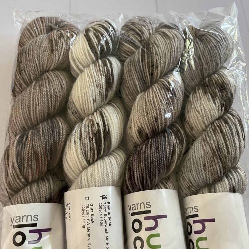 4 Mini skeins of fingering weight yarn in white with black and gray speckles in a clear bag.