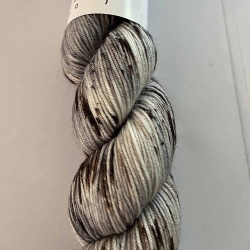 A mini skein of fingering weight yarn in white with black and gray speckles.