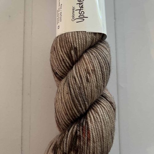 A mini skein of fingering weight yarn in white with black and gray speckles.