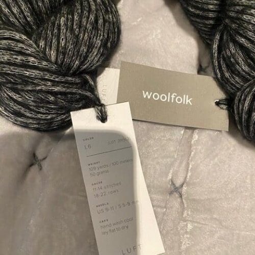 A skein of charcoal yarn with a Woolfolk tag.