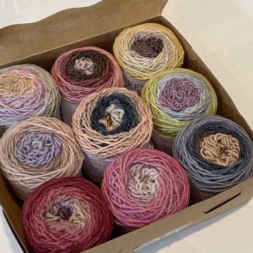 A set of 9 cakes of hand painted yarns in various muted ombre colors.