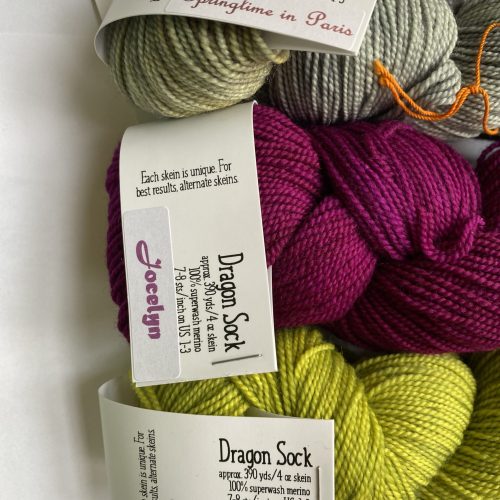 3 skeins of purple, green and variegated gray yarn with shawl pattern.