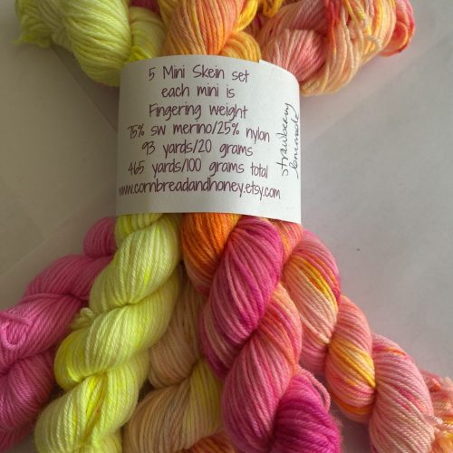 Five mini skeins of pink, orange, and yellow yarn.