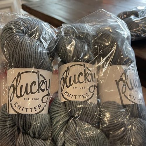 Skeins of gray Plucky Knitter yarn in a clear bag.